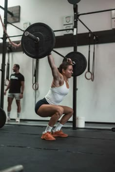 a woman doing squats with a barbell in a crossfit gym area