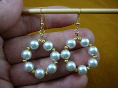 a person holding a pair of gold and white pearls in front of a knitting needle