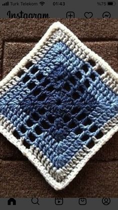 a blue and white crocheted square on top of a brown brick wall,