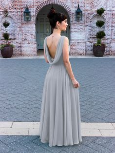 a woman in a long gray dress standing on a brick walkway with her back to the camera