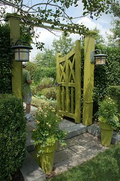 a man standing in front of a green gate surrounded by potted plants and trees