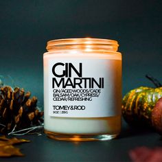 a candle that is sitting next to some pine cones and pumpkins on a table