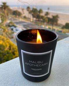 a candle that is on top of a table next to some trees and the ocean