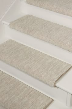 carpeted stair treads on the side of a white staircase with beige rugs