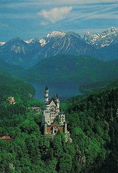 an old castle sits on top of a hill in the middle of mountains with snow capped peaks