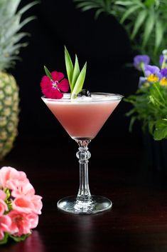 a drink in a wine glass on a table next to flowers