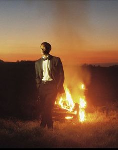 a man in a tuxedo standing next to a car on fire