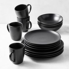 a stack of black plates and cups sitting next to each other on a white surface