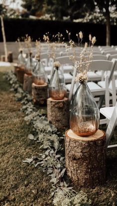 an outdoor ceremony set up with white chairs and vases filled with flowers on top of logs