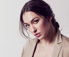 a woman wearing a tan blazer posing for a photo in front of a white background