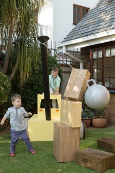 two young boys playing in the yard with wooden blocks, balls and other things on display