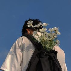 a person with flowers in their hair and a black bag on his back, against a blue sky