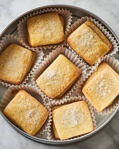 several square pieces of cake sitting in a metal pan on a marble counter top with powdered sugar sprinkled over them