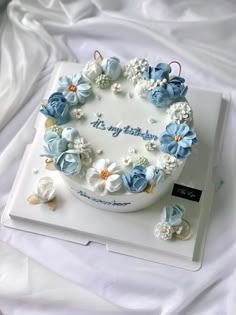 a birthday cake decorated with blue flowers and pearls on top of a white sheet covered bed