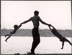 two people jumping into the air while standing on surfboards in front of a body of water