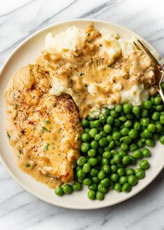 a white plate topped with chicken, mashed potatoes and green peas next to a fork