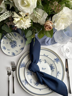 a table set with blue and white plates, silverware and flowers in vases