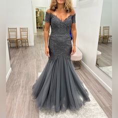 a woman standing in front of a mirror wearing a grey dress with off the shoulder sleeves