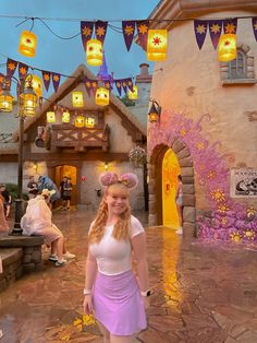 a woman is standing in front of a building with lights hanging from it's roof