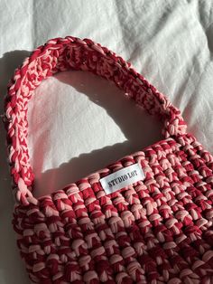 a red and white woven bag sitting on top of a bed next to a pillow