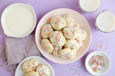 there are some cookies on the table with milk and sprinkles next to them