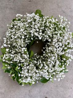 a wreath with white flowers and green leaves on the ground, top view from above