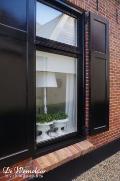 a window with black shutters and a lamp on the side of it in front of a brick building