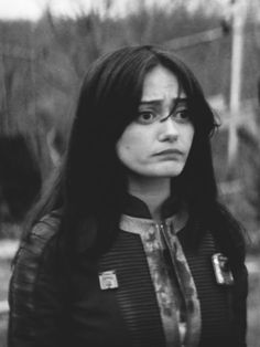 a black and white photo of a woman with long dark hair wearing a shirt that has patches on it