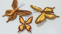 three wooden butterflies are sitting on a white surface, one is yellow and the other is red