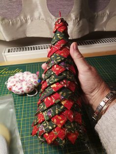 a person is holding up a christmas tree made out of wrapping paper and scissors on a cutting board