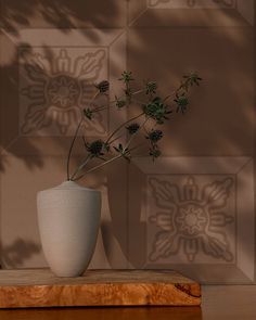 a vase with some flowers in it sitting on a wooden table next to a wall