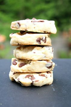 a stack of chocolate chip cookies sitting on top of a black table next to a green tree