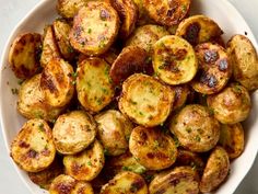 a white bowl filled with cooked potatoes and parsley on top of a marble table