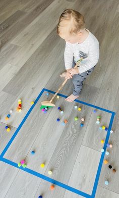 a toddler is playing with colored balls on the floor in front of a blue square