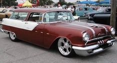 an old red and white car parked in a parking lot next to other antique cars