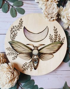 a wooden plaque with an image of a moth on it and flowers in the background