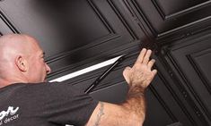 a man in black shirt and white pants working on a door with an electric screwdriver