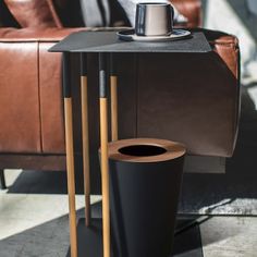 a black table with two wooden legs and a cup on it next to a brown leather couch