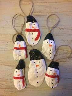 four snowmen are hanging from twine strings on a wooden surface, one is black and the other is white