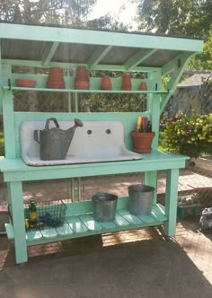 an outdoor sink with potted plants on the top and shelves above it, in front of a chain link fence