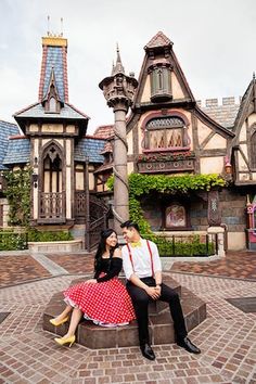 a man and woman sitting on top of a bench in front of a castle like building