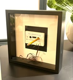 an electrical device in a frame on a table next to a potted green plant