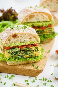 two sandwiches with lettuce, tomato and avocado on a cutting board