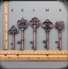 six antique keys are shown in front of a measuring ruler with the word e klma on it