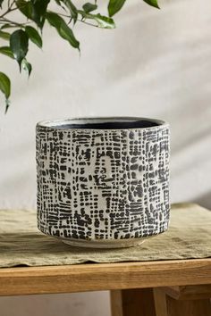 a black and white pot sitting on top of a wooden table next to a plant