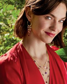 a woman in a red dress is smiling and wearing gold jewelry with green leaves around her neck