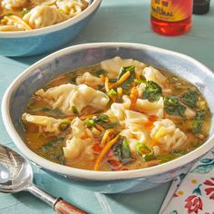 two bowls filled with dumplings and vegetables on a blue tablecloth next to a spoon