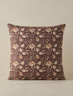 a brown and white pillow with floral designs on it's side, sitting on a table