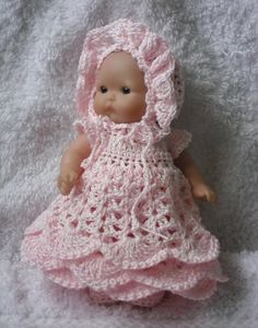 a small doll wearing a pink dress and bonnet on top of a white bed sheet