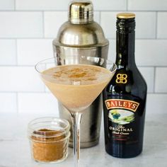 an alcoholic drink in a martini glass next to a bottle of bailey's